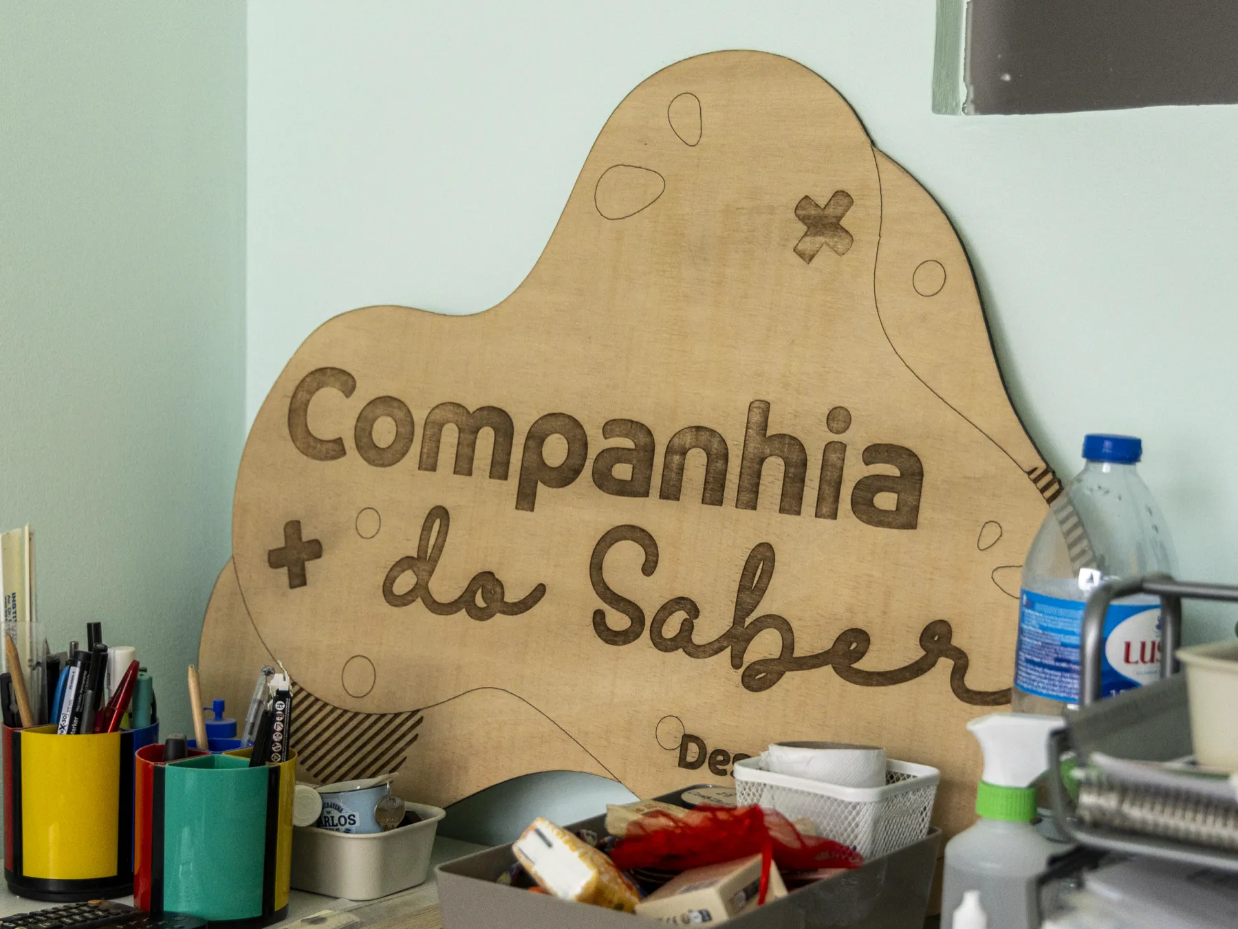 Placa de madeira gravada com o nome Companhia do Saber, sobre a secretária