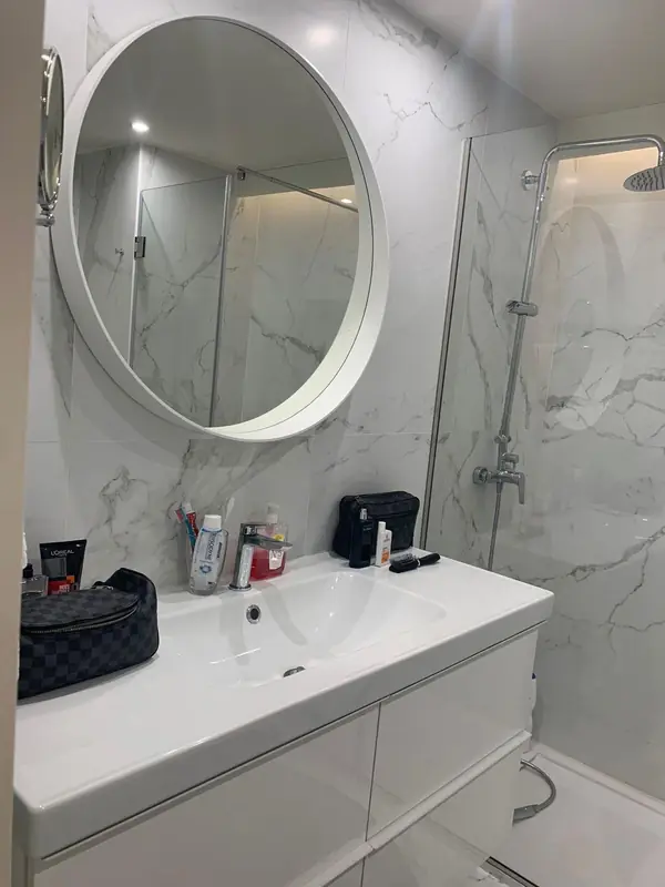 White marble bathroom with a round white framed mirror
