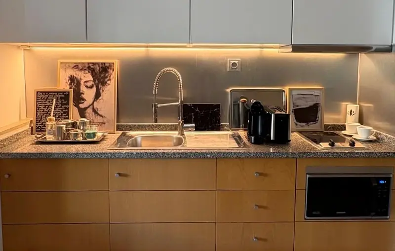 Kitchenette with a granite counter, warm under cabinet light and black and white portraits