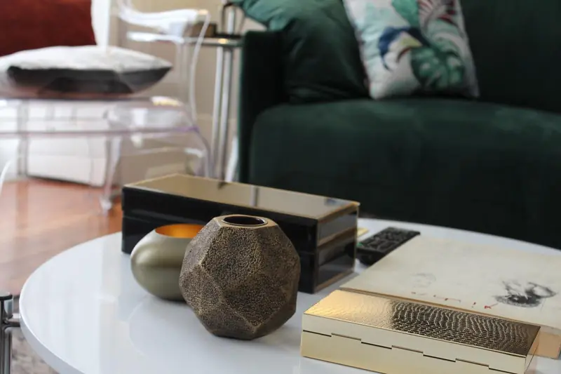 Mesa branca com vaso geométrico em bronze diante de um sofá de veludo verde