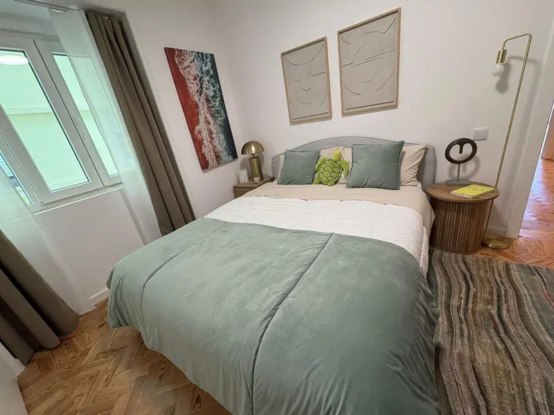 Quarto com colcha verde-salva, candeeiro de latão, tapete listrado e fotografia de costa