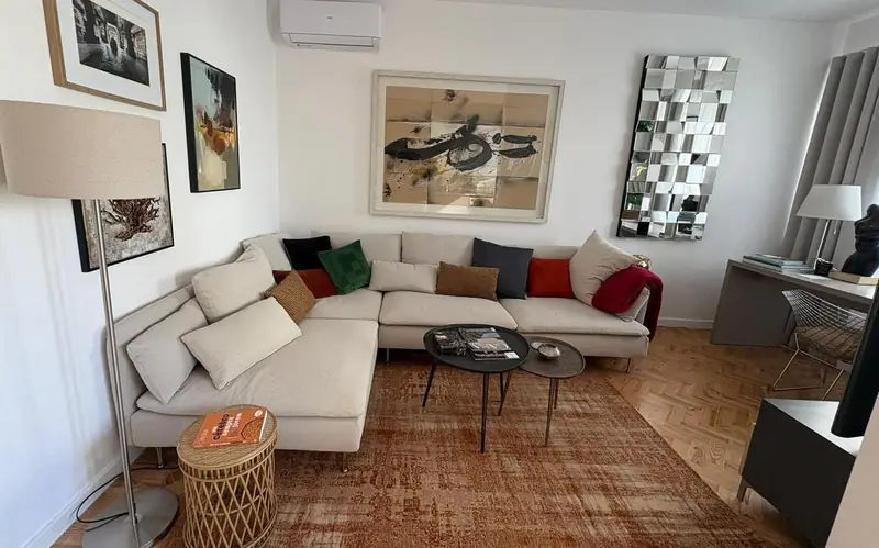 Sala com soalho em espinha, tapete cor de tijolo, espelho facetado e candeeiro de pé