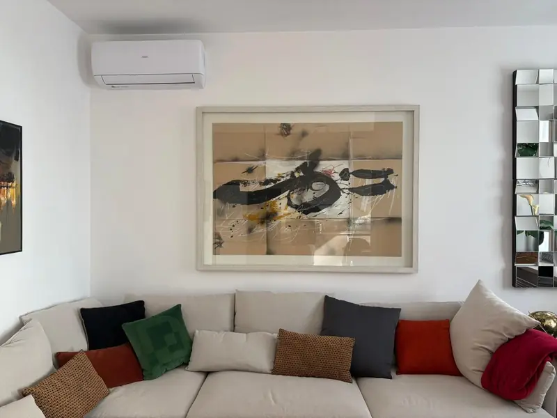 Sofá de canto claro com almofadas vermelhas, verdes e negras sob pintura caligráfica
