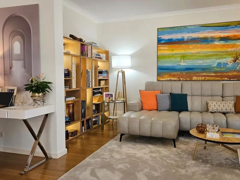 Sala com estante de madeira iluminada, sofá capitonê e pintura de faixas coloridas