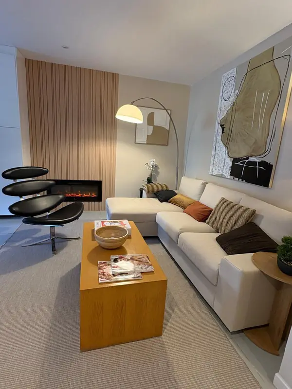 Vista de conjunto da sala com cadeira escultórica negra, mesa baixa de madeira e parede ripada