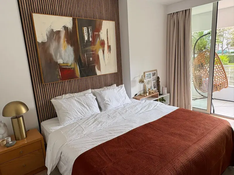 Quarto com cabeceira ripada, pintura abstrata em tons de terra e colcha cor de ferrugem