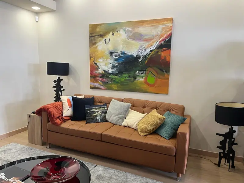 Sofá de pele caramelo com almofadas coloridas sob pintura abstrata de grande formato