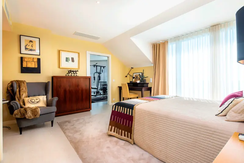 Quarto de paredes amarelas com cómoda de madeira escura, cadeirão e manta às riscas