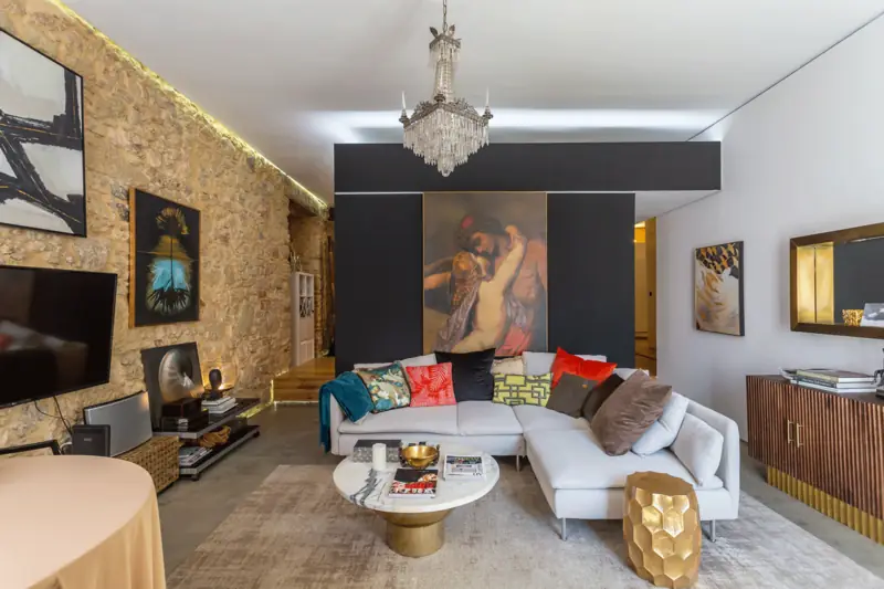 Sala com sofá de canto branco, pintura clássica sobre painel negro e mesa de mármore com pé dourado