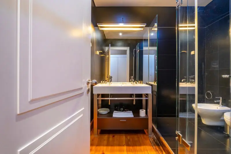 Black walled bathroom with a washbasin on a timber stand and golden light