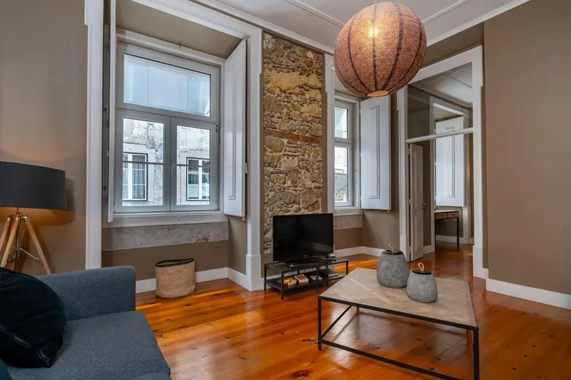 Sala com soalho de pinho, pedra à vista entre janelas, candeeiro de fibra e mesa de ferro