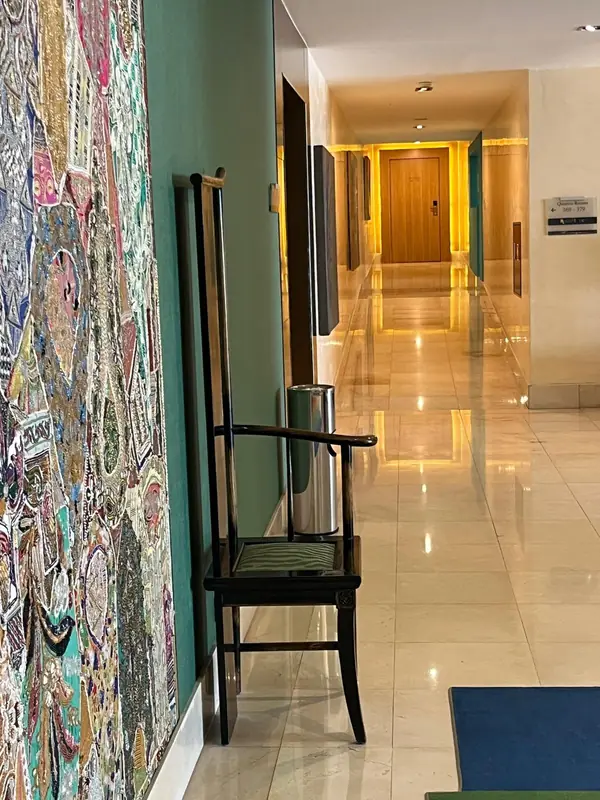 Corredor de mármore com tela bordada, cadeira de espaldar alto e parede verde