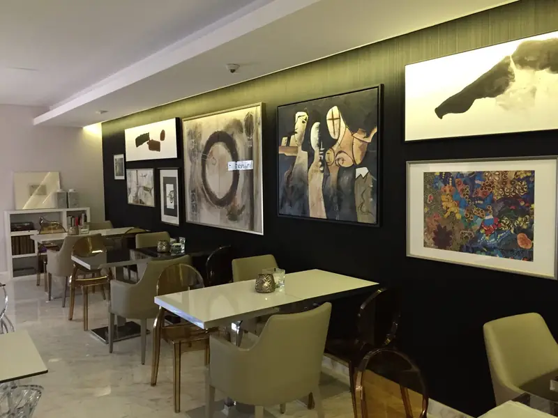 Sala de refeições com parede negra coberta de arte e mesas brancas