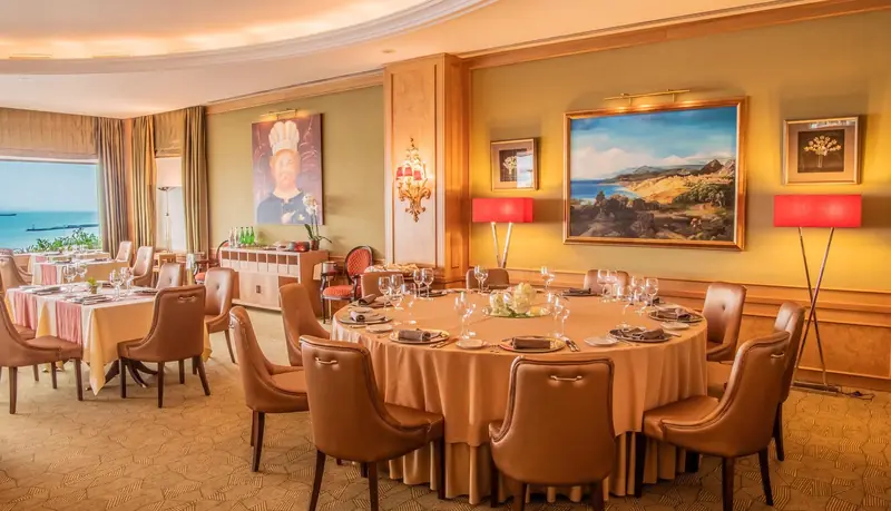 Sala de restaurante com mesa redonda posta, cadeiras de pele e candeeiros vermelhos