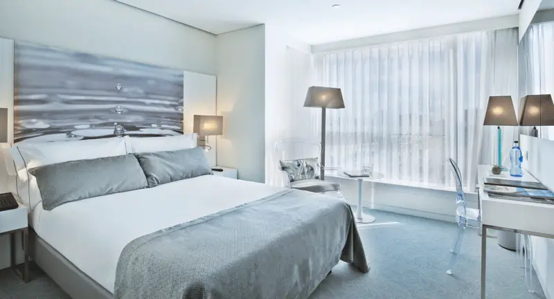 Quarto em cinzentos suaves com cabeceira fotográfica de mar e cortinas translúcidas