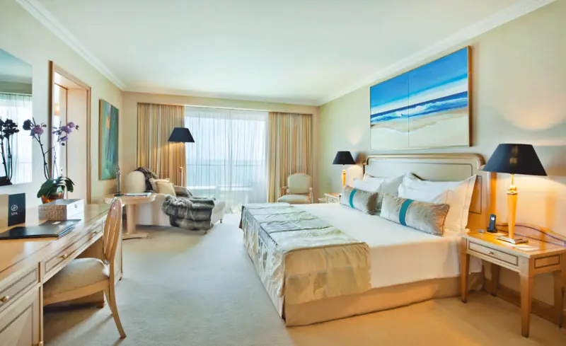 Quarto com pintura azul sobre a cabeceira, orquídeas e zona de estar junto à janela