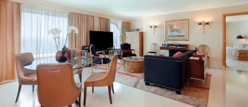 Sala de suite com cadeiras de pele caramelo, sofá azul-marinho e janelas corridas
