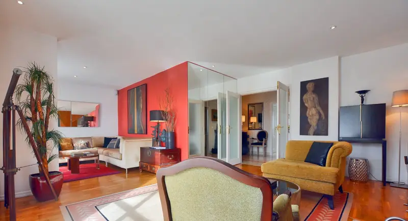 Sala com parede vermelha, porta espelhada, sofá mostarda e madeira escura