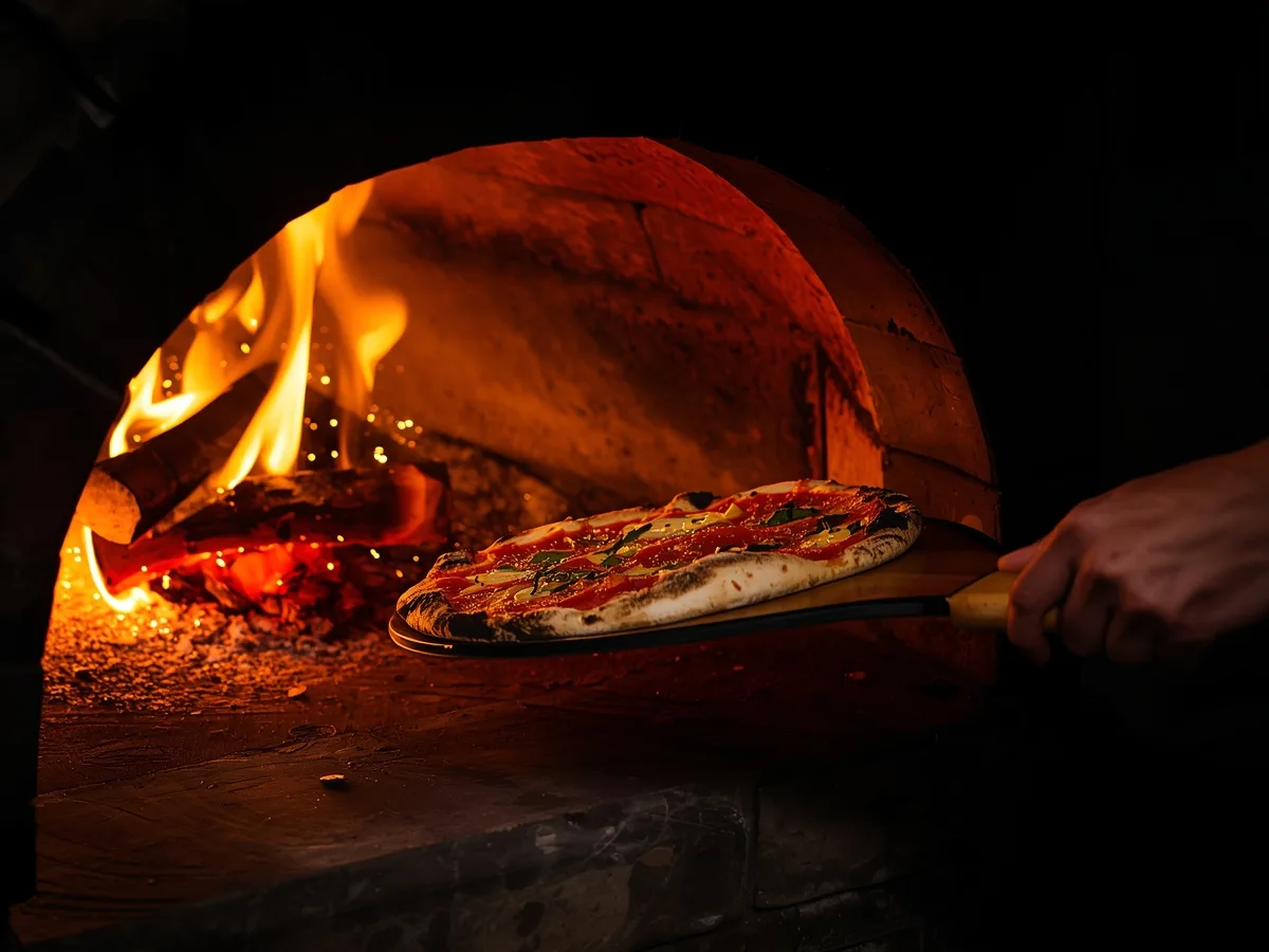 Pizzaiolo a enfornar uma pizza com a pá de madeira, entre chamas