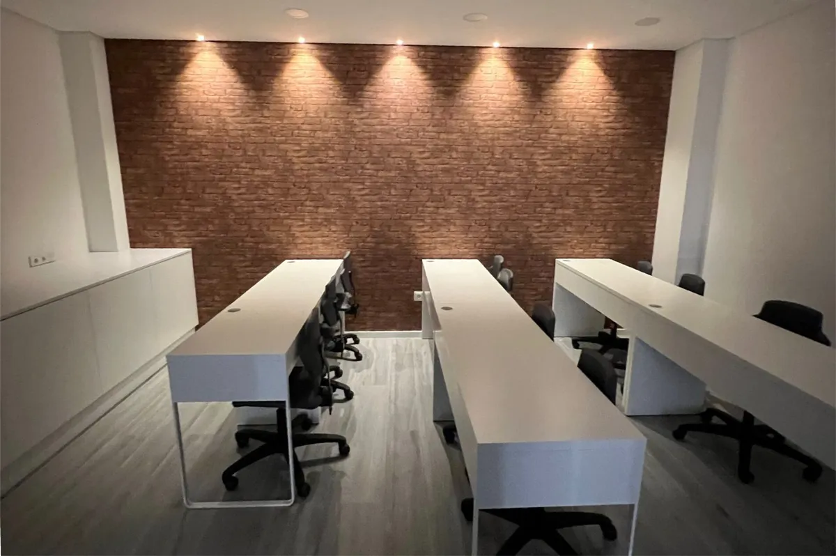Auditório com filas de mesas brancas e parede de tijolo iluminada